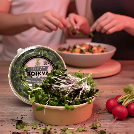 A couple preparing a healthy dinner by adding spicy MOĆNO radish microgreens to a fresh salad, with whole radishes in the background.