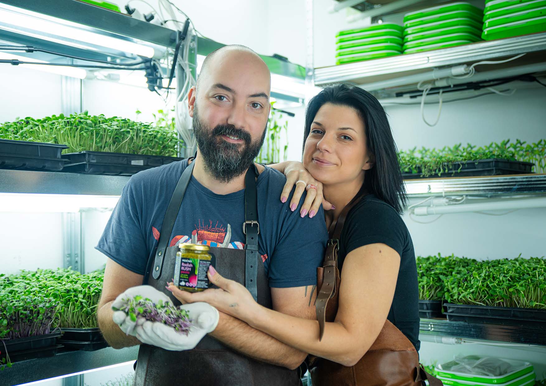 Ivan and Milena in the MOĆNO vertical farm, holding Radish Rush pesto and fresh microgreens