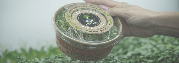 A hand holding a MOĆNO Vitamin Mix microgreens cup in bio-packaging