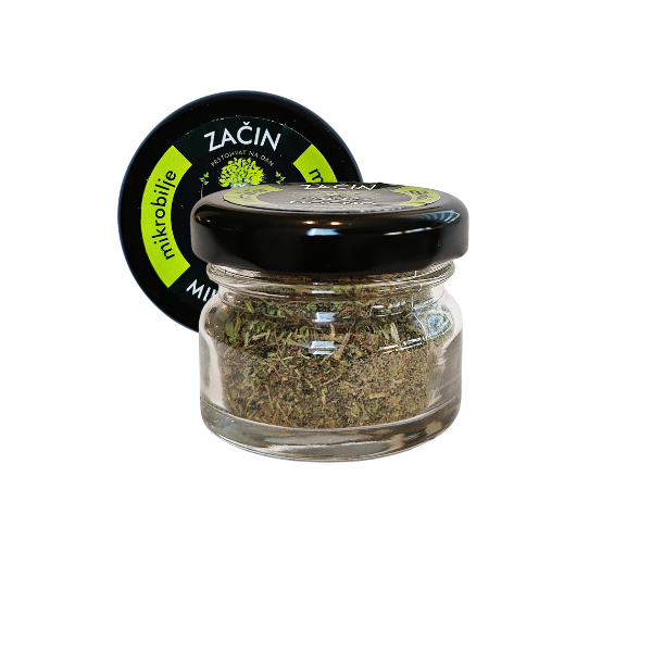Central view of a small glass jar of MOĆNO dried Basic spice. Clearly visible black label with white and green details, while finely chopped dried microgreens can be seen through the glass.