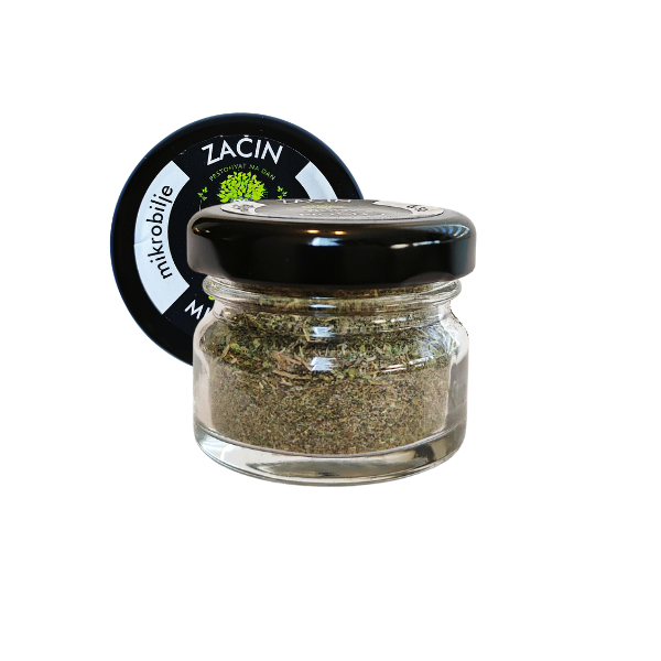 Central view of a small glass jar of MOĆNO dried spice with added sea salt. Clearly visible black label with green details and crystal salt texture mixed with dried microgreens inside the jar.