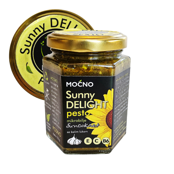 Central view of a hexagonal glass jar of Sunny Delight pesto spread. Clearly visible black label with sunflower illustration and golden lid with a yellow "Sunny Delight" sticker.